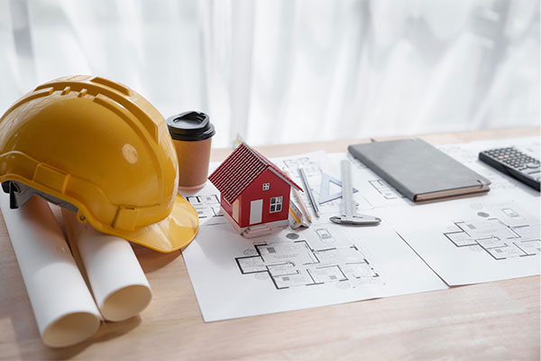 Image: Red color toy model house and yellow hard hat on top of engineering architect blueprint