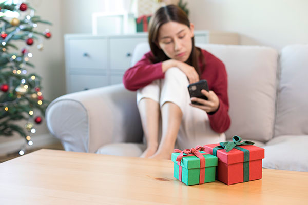 Image: Woman sits on a sofa with gift box, christmas tree in the background