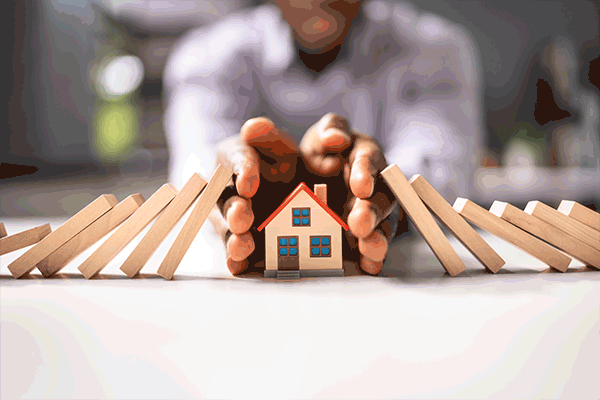 Image: Hands protecting a small model home from dominos