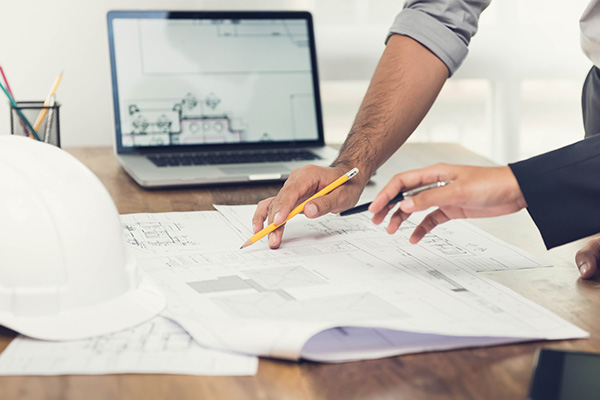 Image: Architect or engineer team discussing a project design using blueprints and a laptop computer at the office before visiting work site.